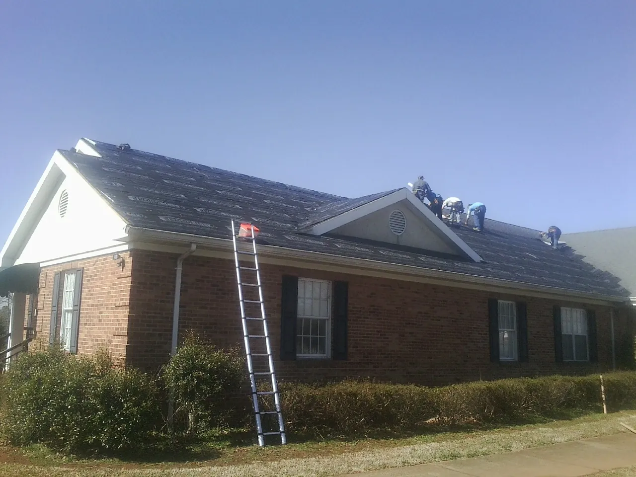 Crew tearing shingles off a brick ranch roof with a ladder set — Metal Roof Repair work by our crew in Milligan