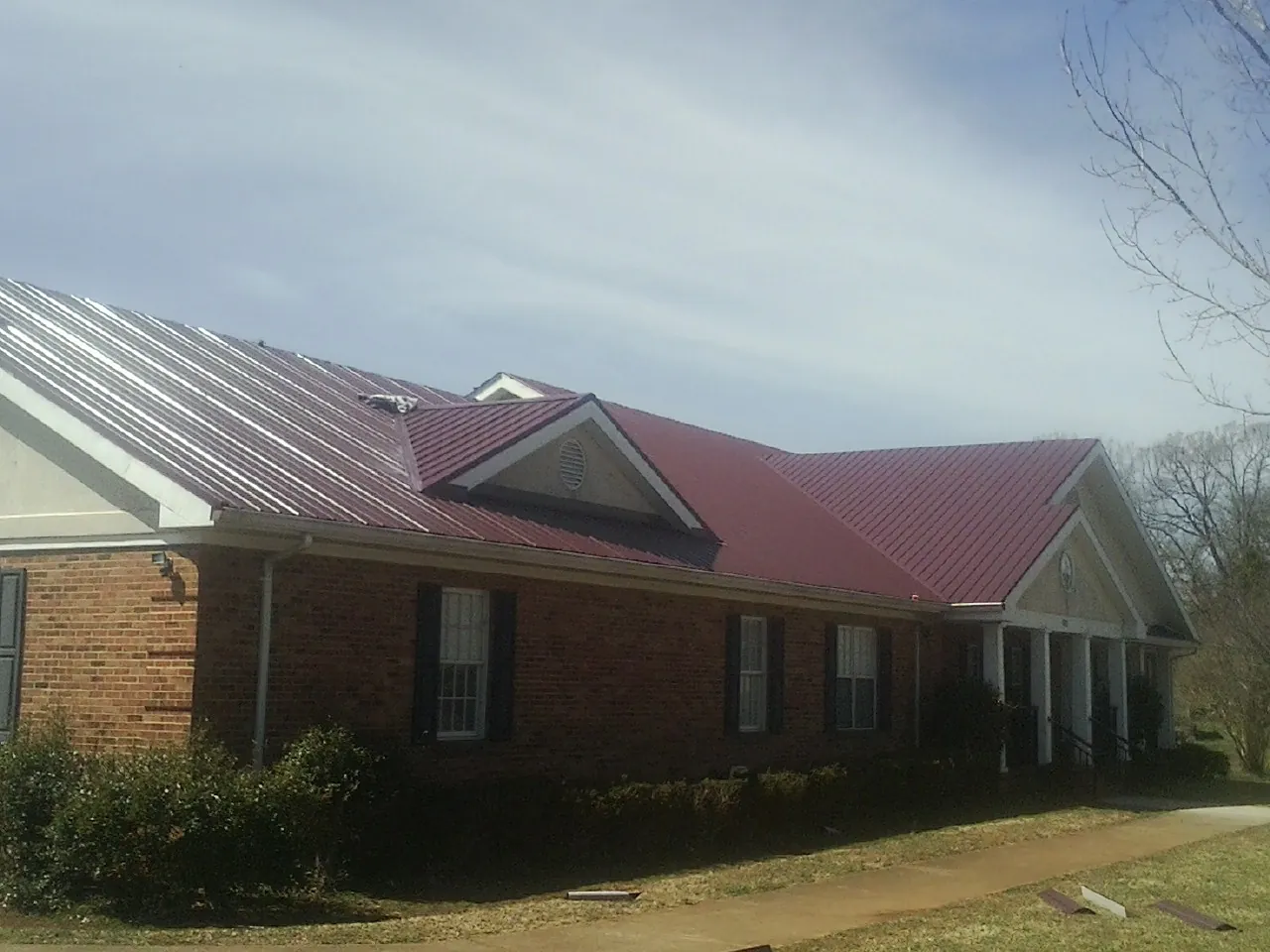 Red metal roof with gabled entries on a long brick building, from a Hail Damage Roof Repair job in Milligan