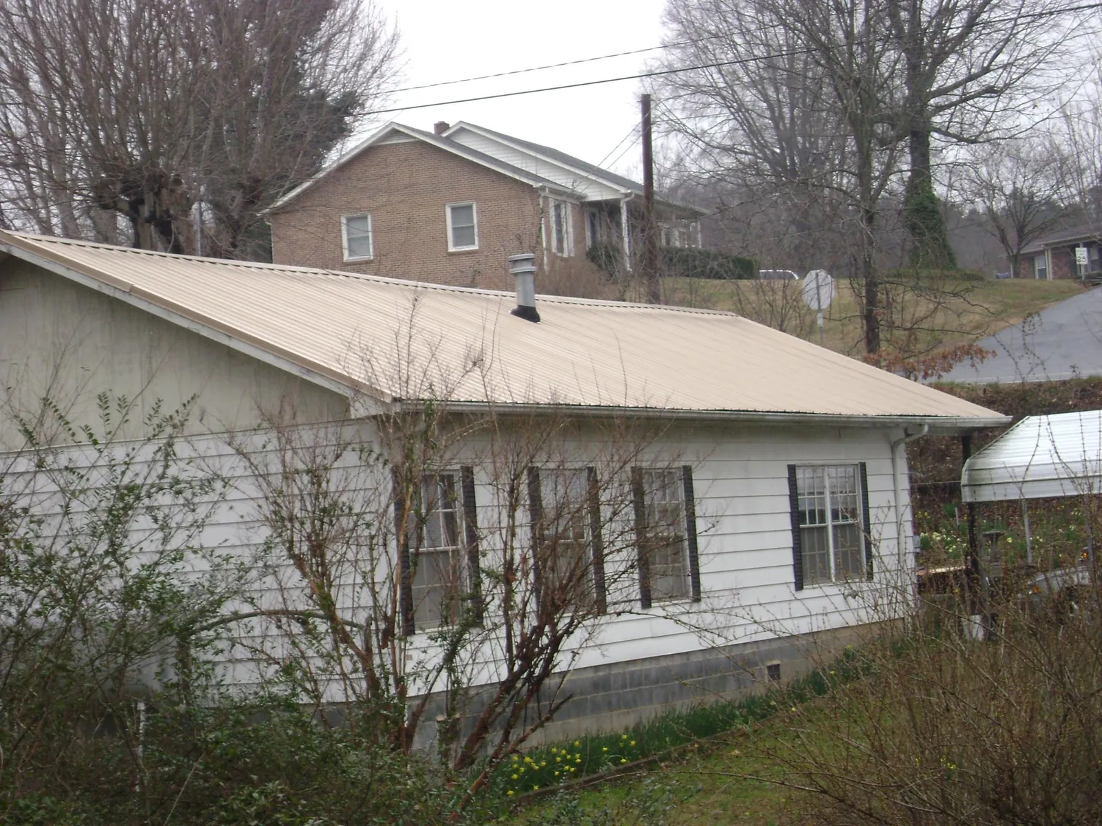 Tan metal roof on a white sided house set into a hillside — Commercial Roofing by Roofing Brothers in Milligan