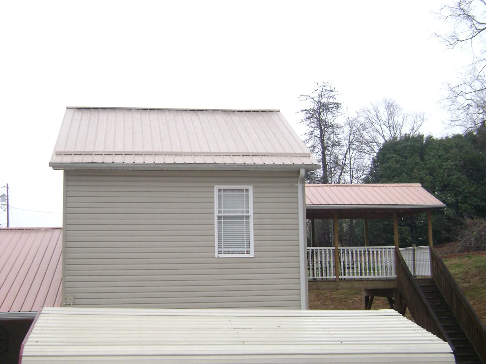 Tan metal roofs on a two story addition and attached porch, from a Roof Replacement job in Milligan